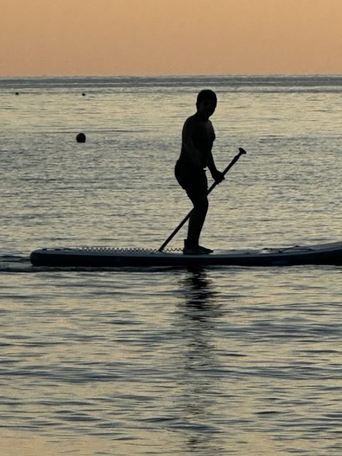 Un ragazzo in piedi su una tavola da SUP al tramonto