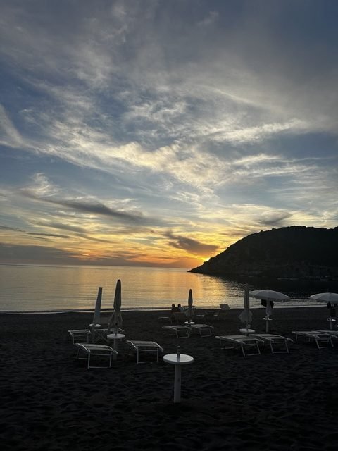 Lettini e ombrelloni chiusi sulla spiaggia al tramonto, con il promontorio di Castrocucco